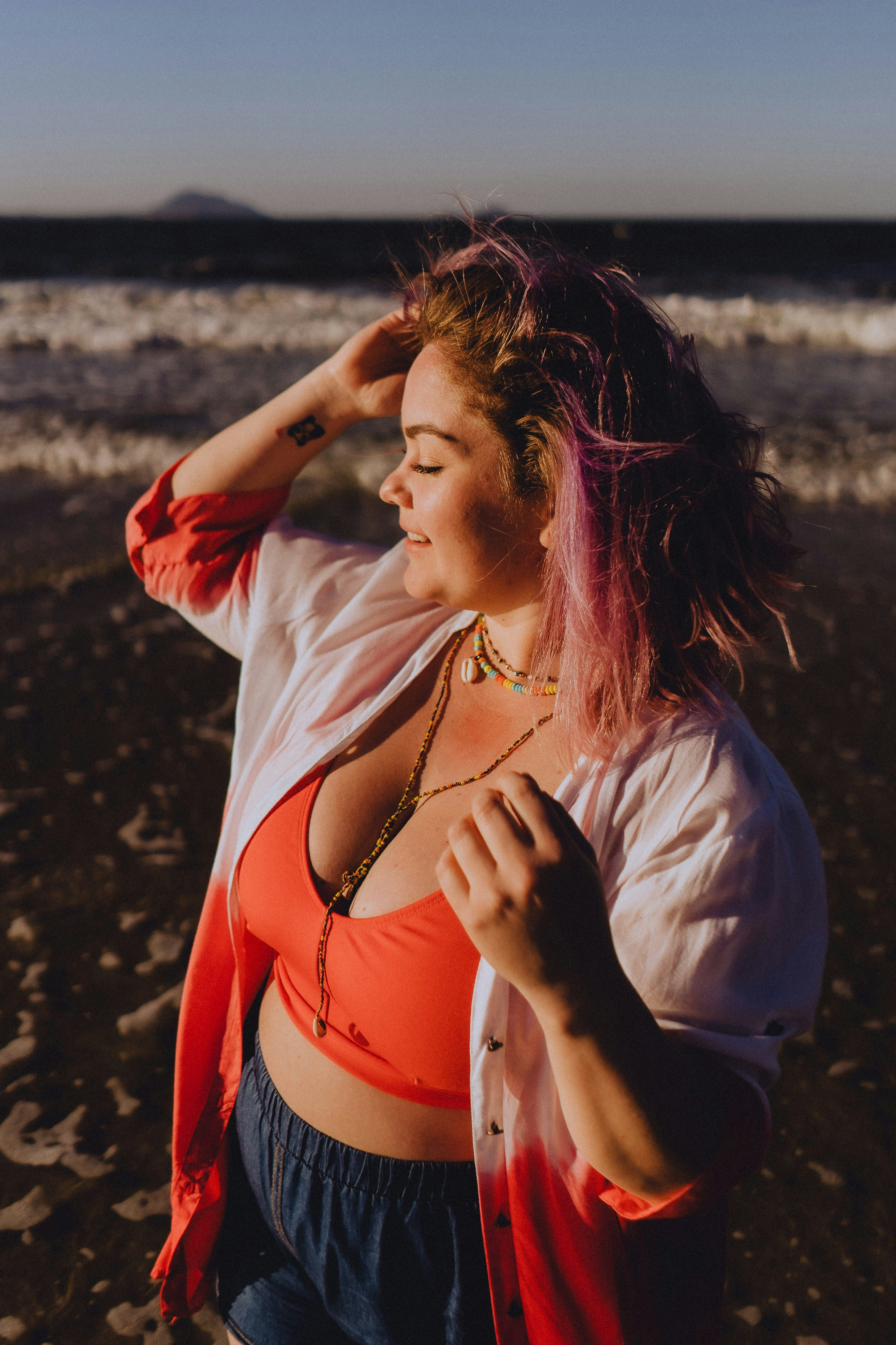 Woman with pink hair standing on a beach at sunset